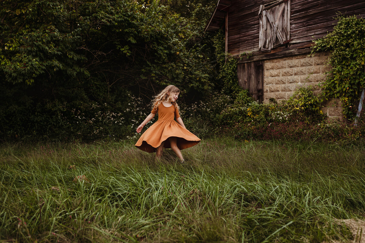 A little girl in an orange dress is twirling in a field.