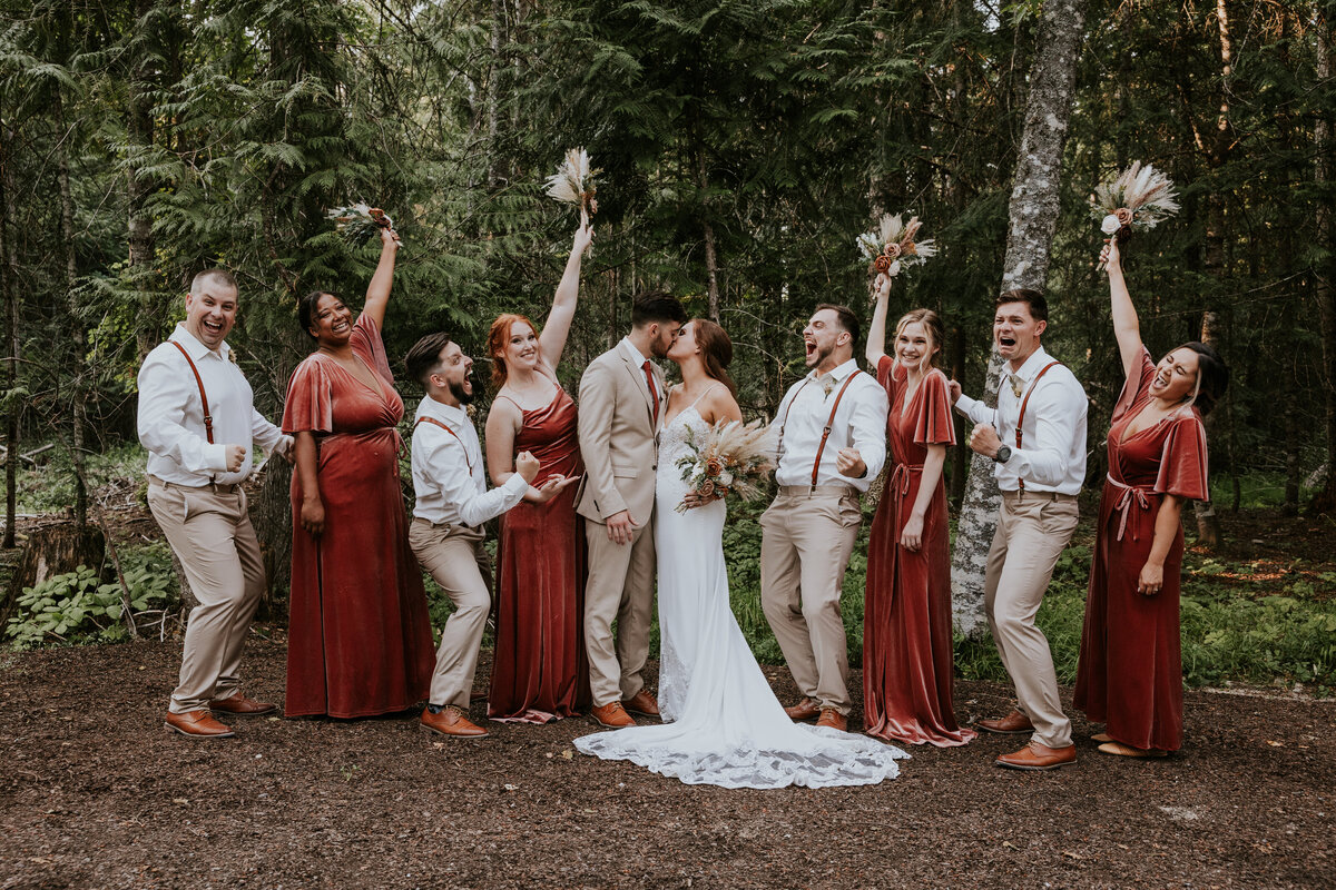 Bridal party celebrates while bride and groom kiss.