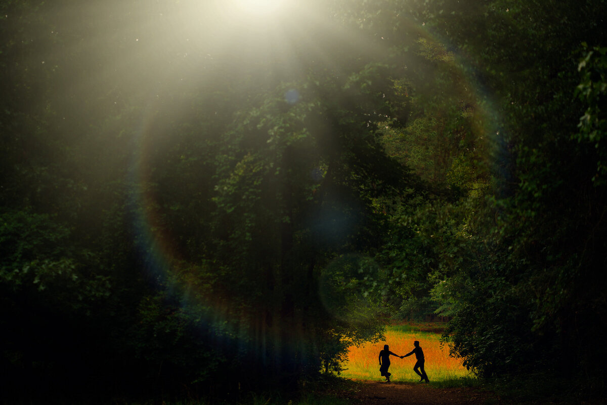 Couple dancing in a forest clearing, with a mesmerizing lens flare illuminating them from above