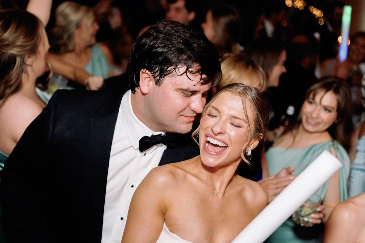 The groom leans in to whisper something to the bride, making her laugh joyfully during the wedding reception.