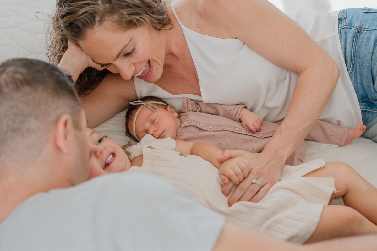 Family of four snuggles in bed during lifestyle family photography with their newborn.