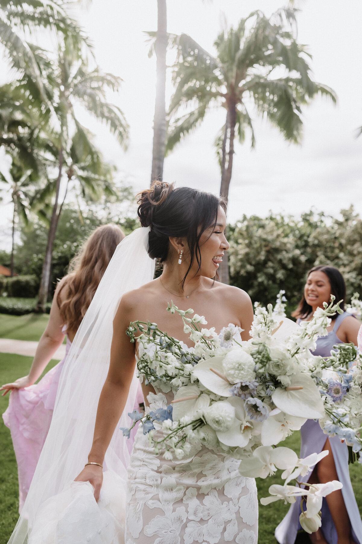 bride laughing with bridesmaids dancing at four seasons oahu, wearing multicolor dresses and holding wedding bouquet