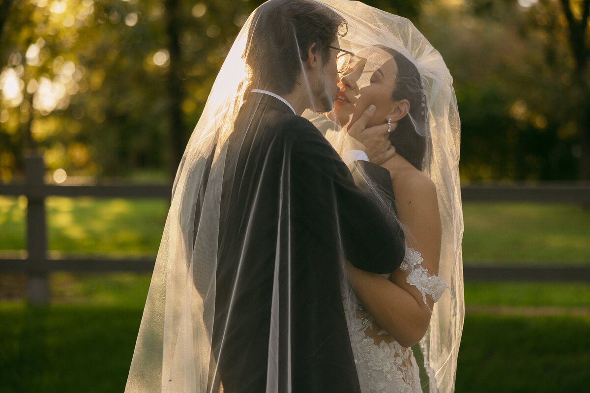 A wedding couple about to kiss as a veil is draped over their heads.