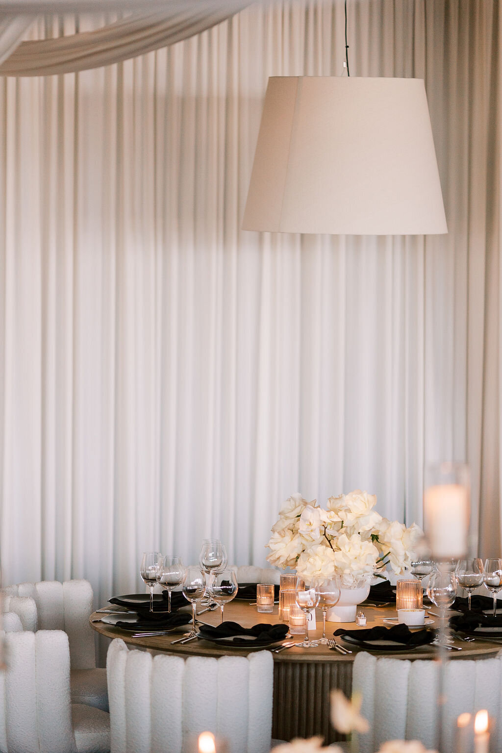 A close-up of a wedding reception table with white flowers, black tableware, and a softly glowing candle.