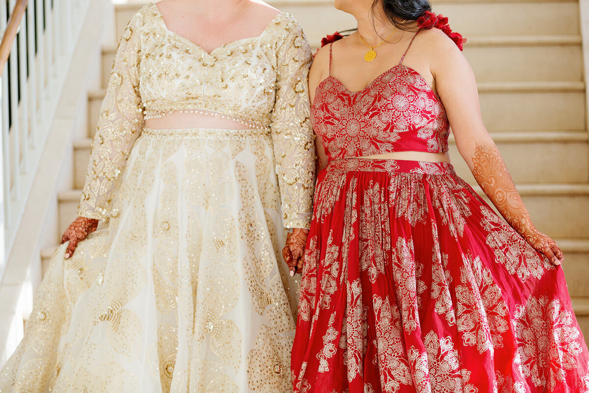 A close up of two intricate wedding dresses as the newlywed couple holds hands 