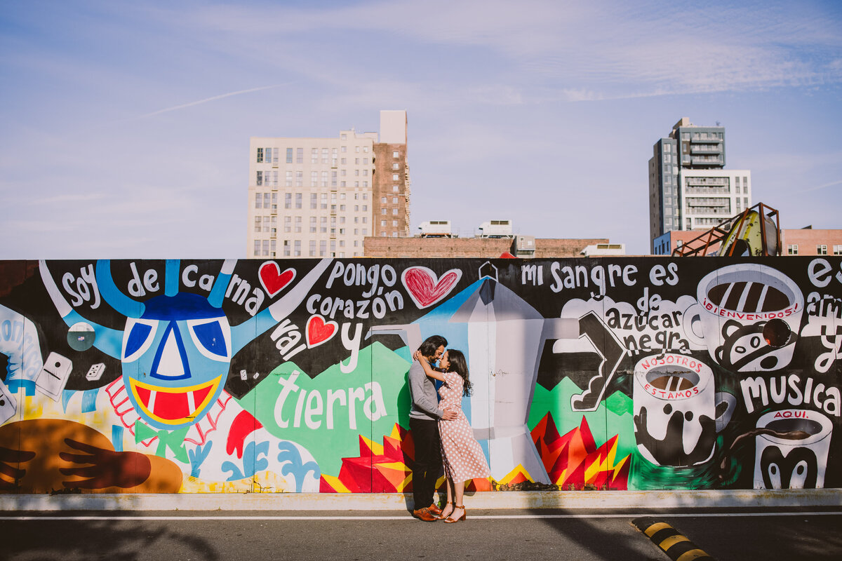 Engaged couple embrace in front of a mural at domino park in brooklyn in nyc
