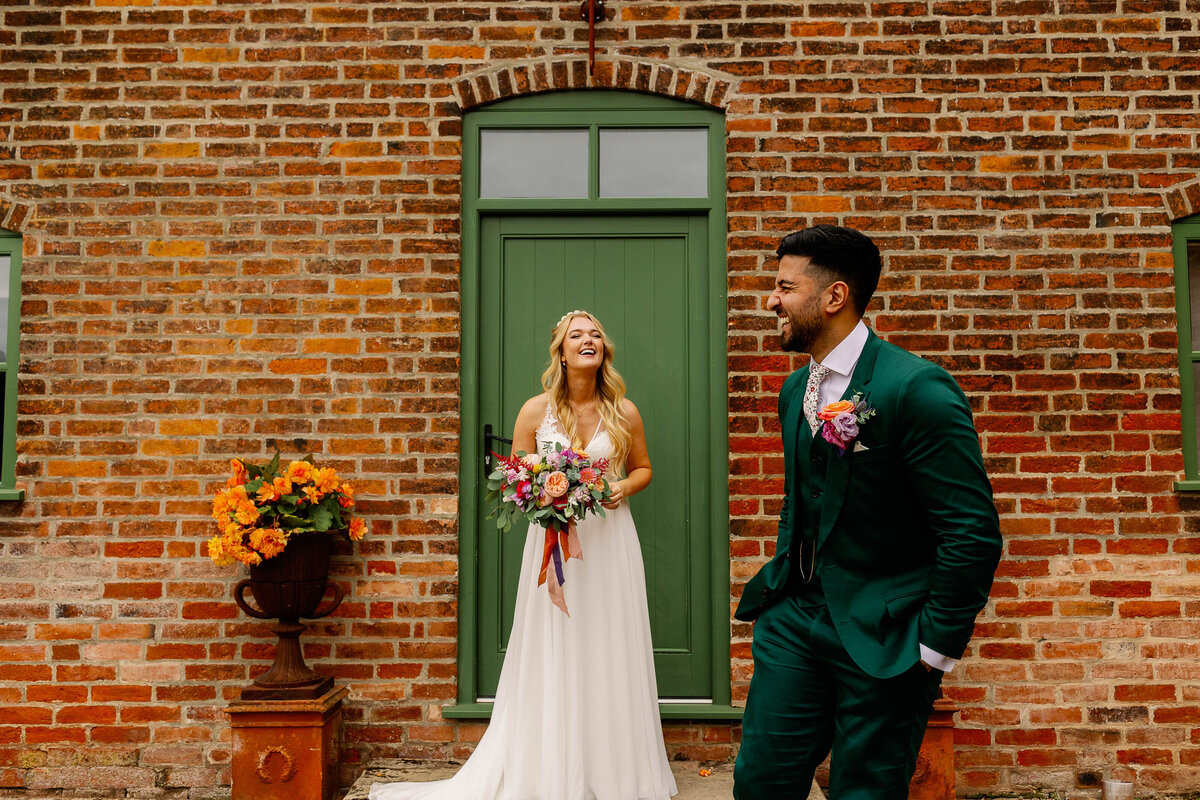 Bride and Groom in green suit stood in front of red brick building at Thorpe Gardens