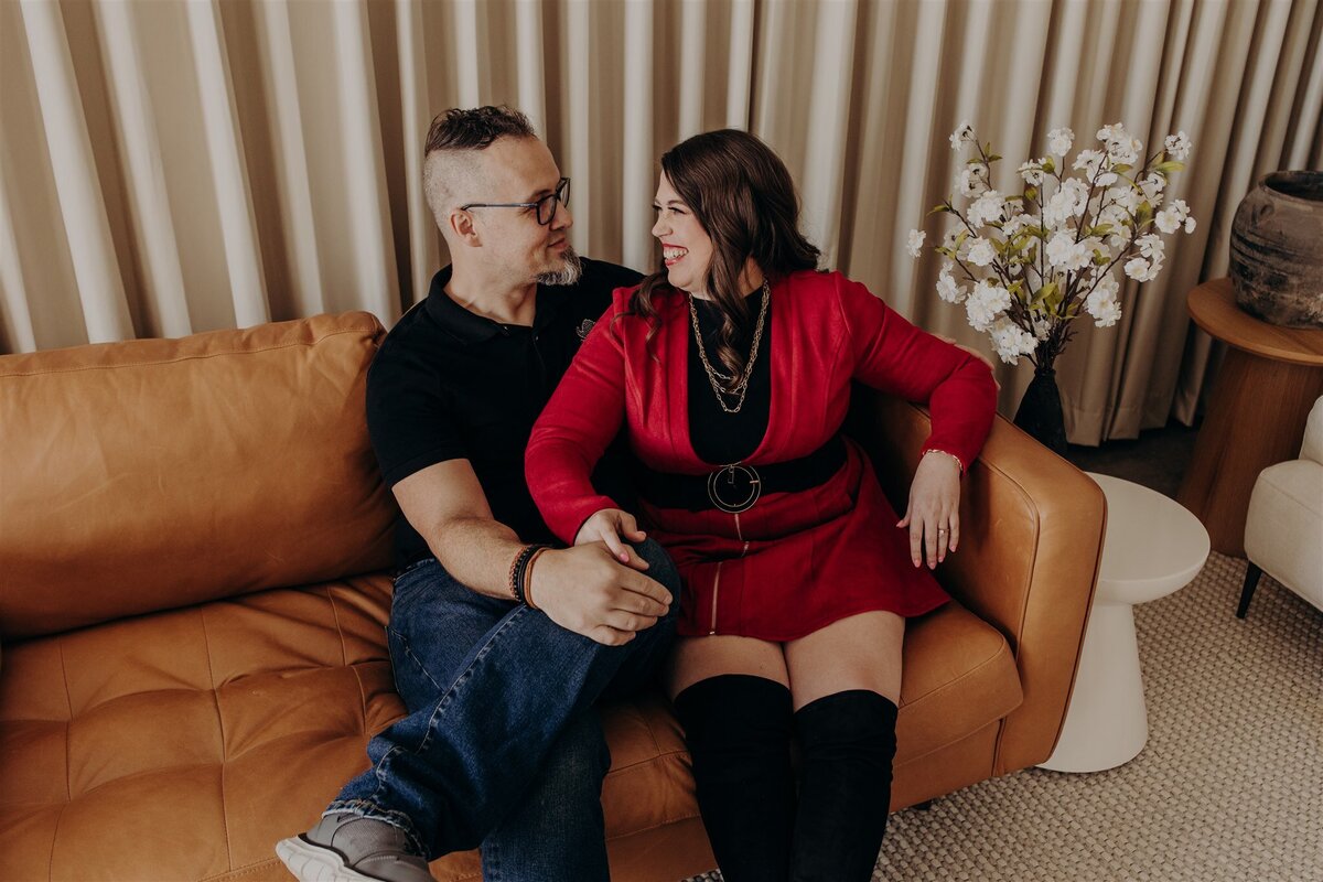 couple on a brown leather couch holding hands and looking into each other's eyes