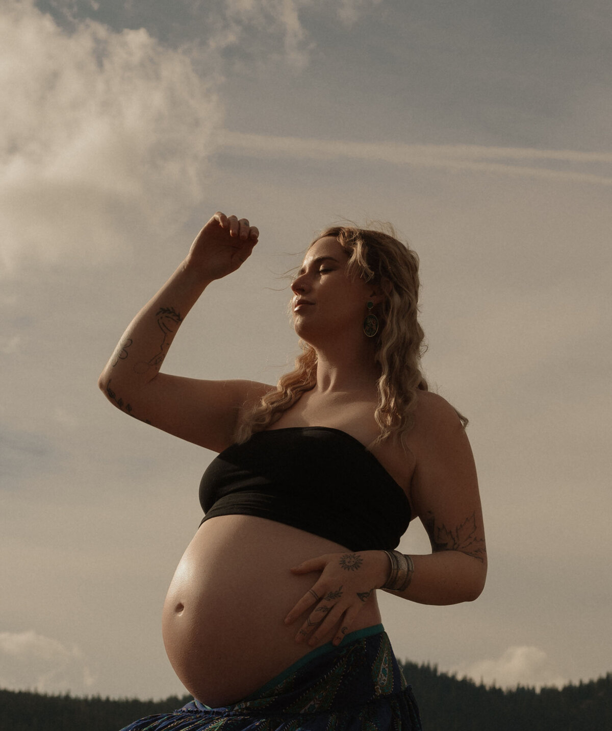 pregnant mother poses in the sun against a blue sky with clouds backdrop in Oregon photoshoot