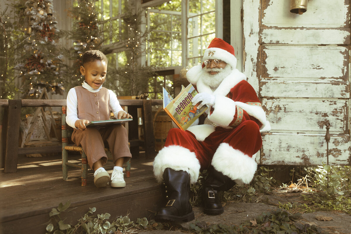 A little boy sitting with The Black Santa of Atlanta while reading a book at Das Hinterhaus.