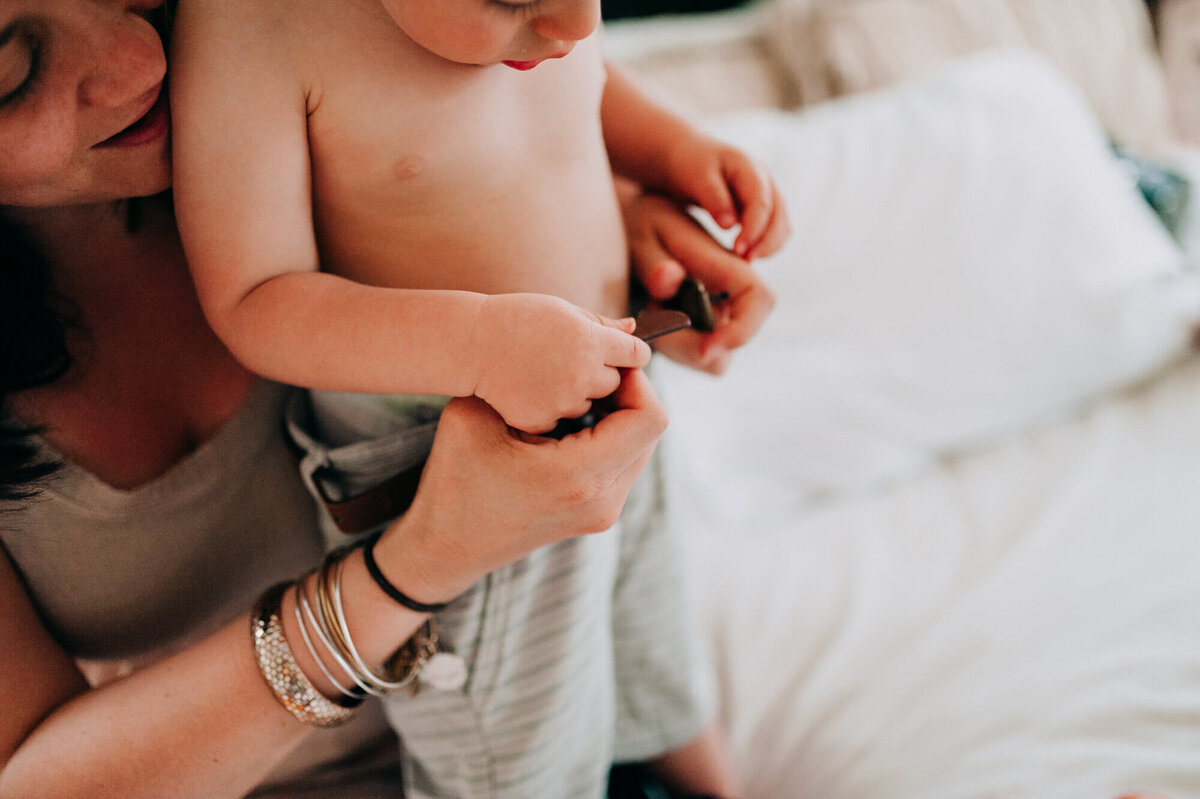 A mother lovingly helps her toddler son put on his belt