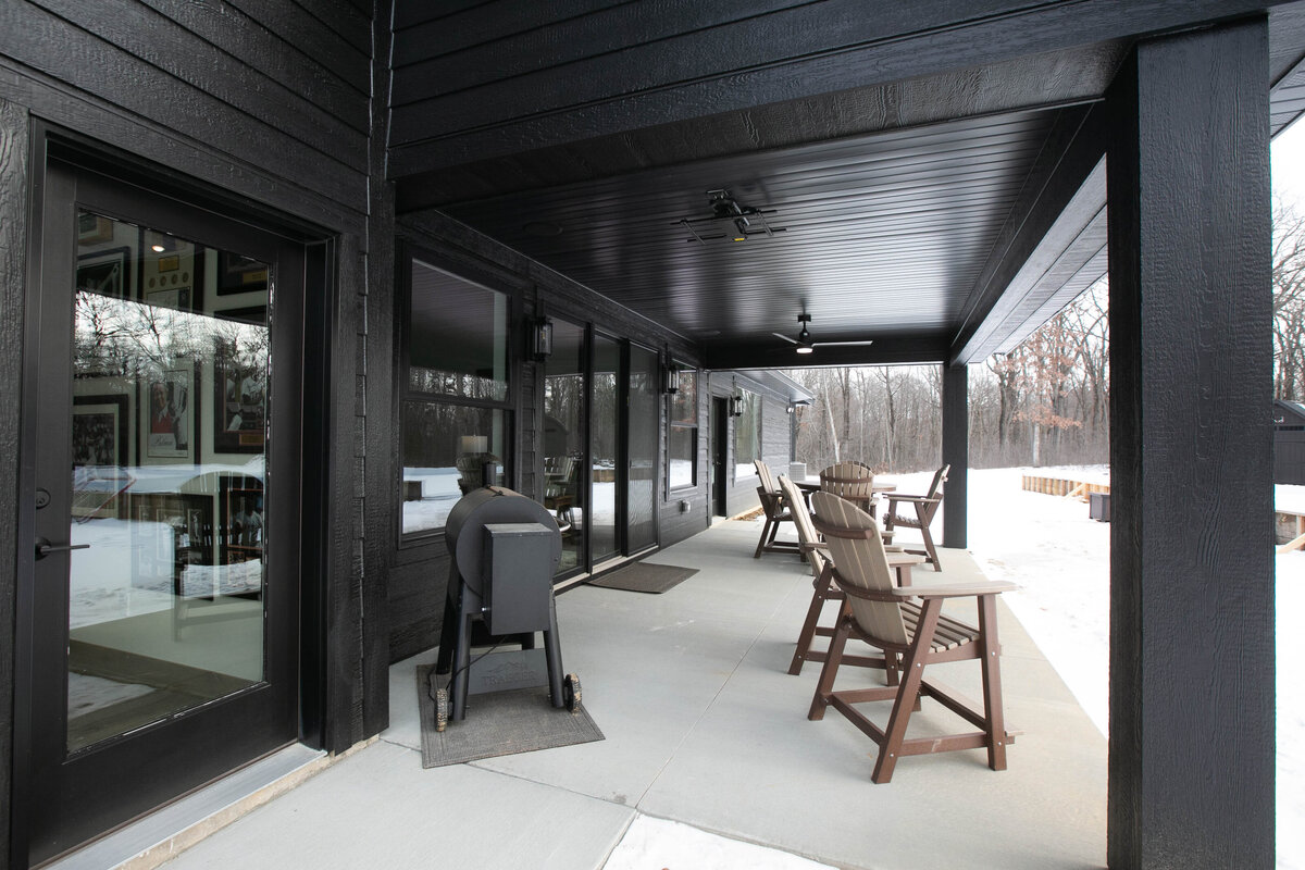 Exterior back view of custom home in Elk River, Minnesota with black siding, wood details and patio built by Cornerstone Custom Builds
