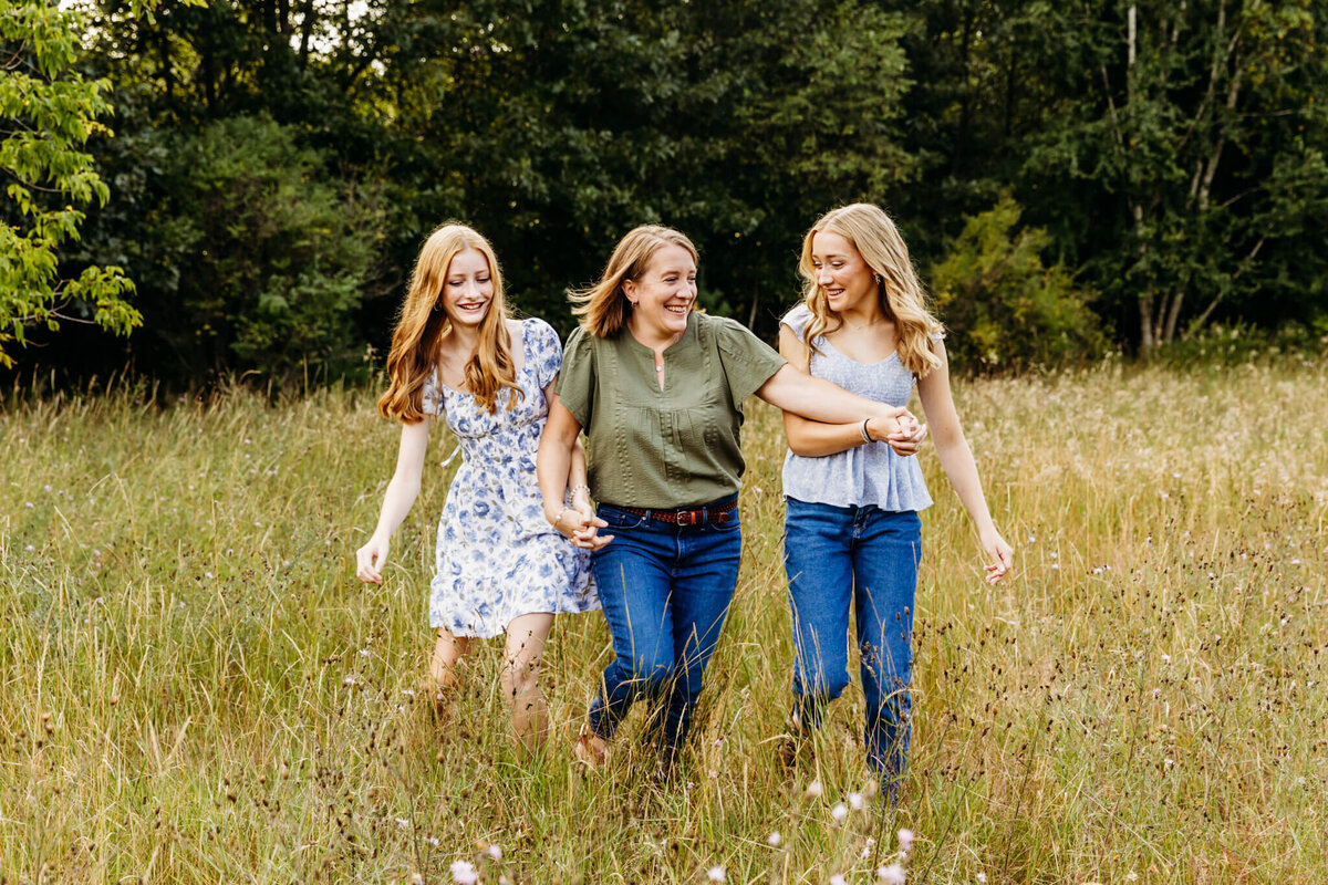 mom and her two daughters holding hands as they walk together and laugh during their Milwaukee family photo session