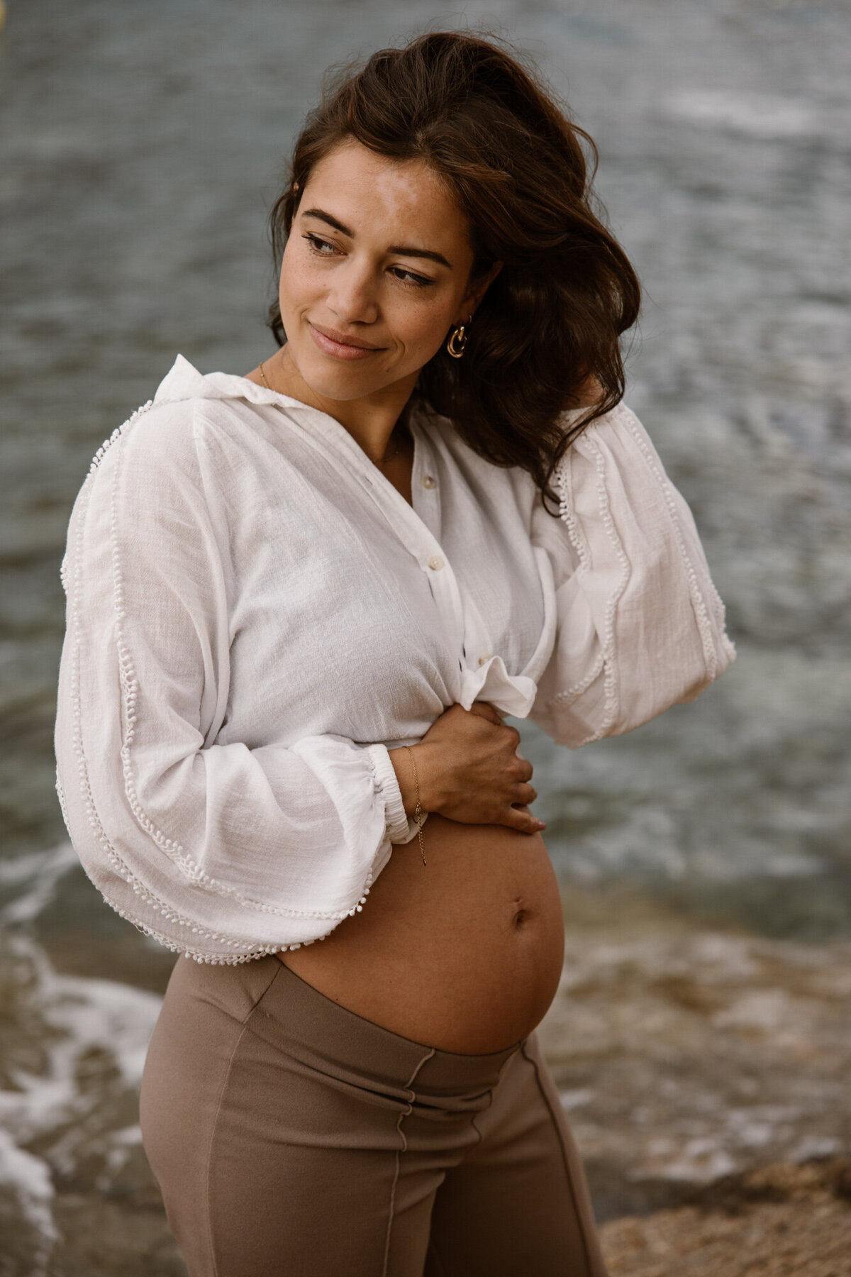 Woman is posing on a beach while going through her hair for her pregnancy shoot on Ibiza