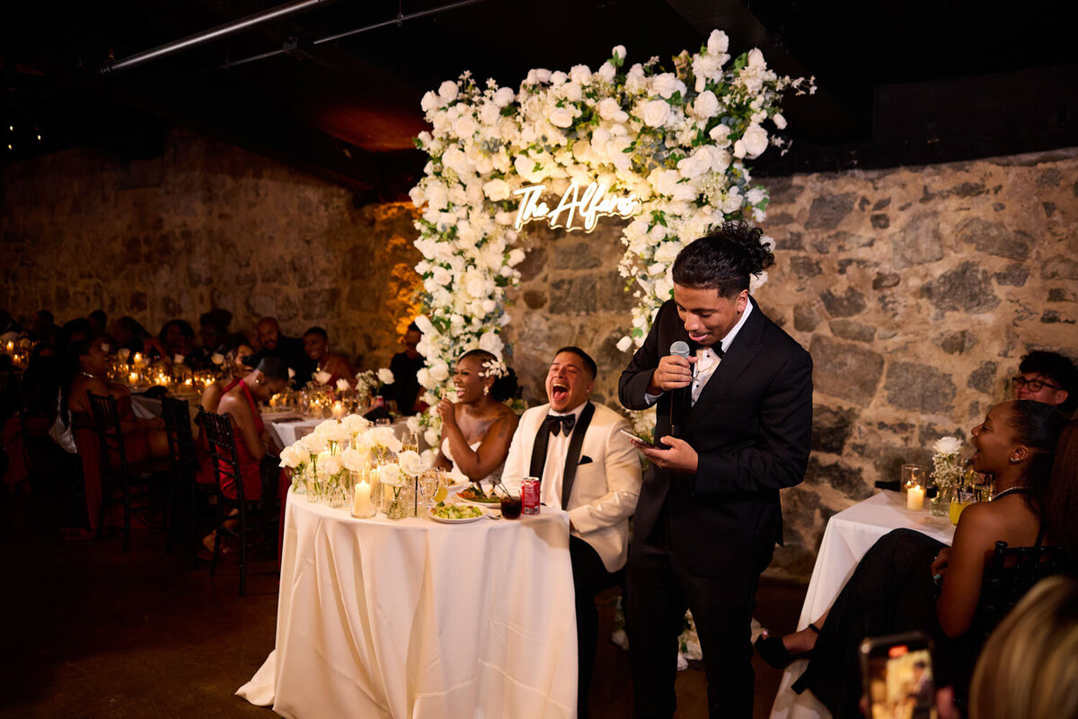 Bride and groom laughing while best man reading his speech