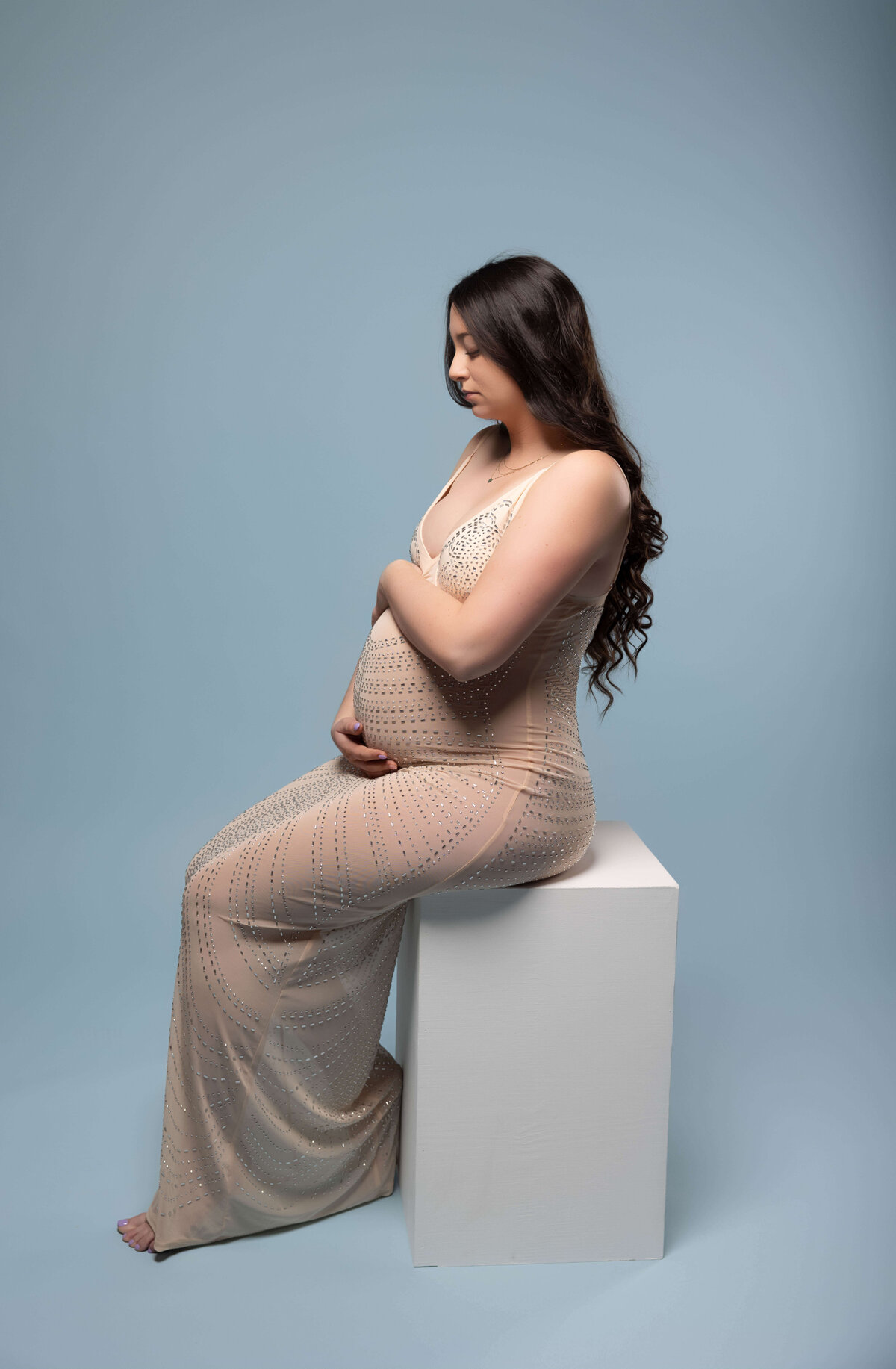 woman sitting on box holding belly in maternity session with reva davis photography