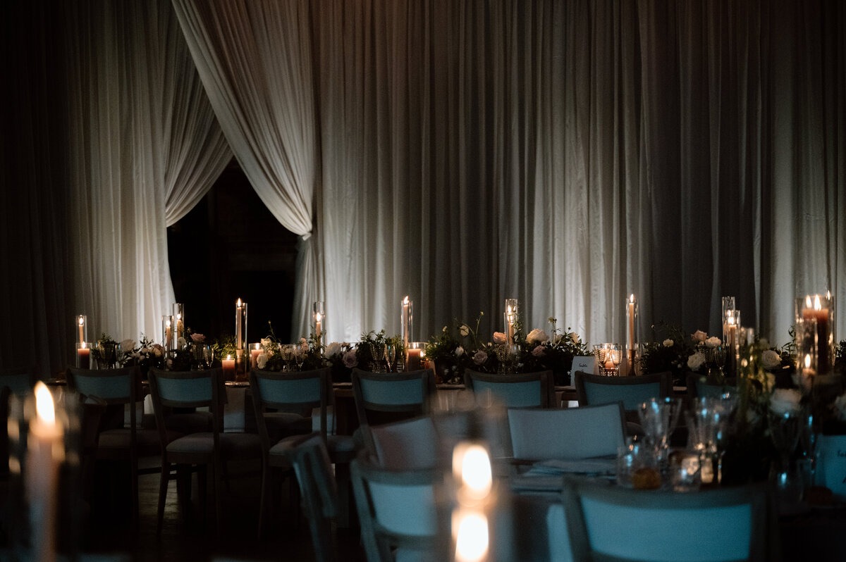 Round table with candles and white floral center piece and luxury drapping in luxury venue.