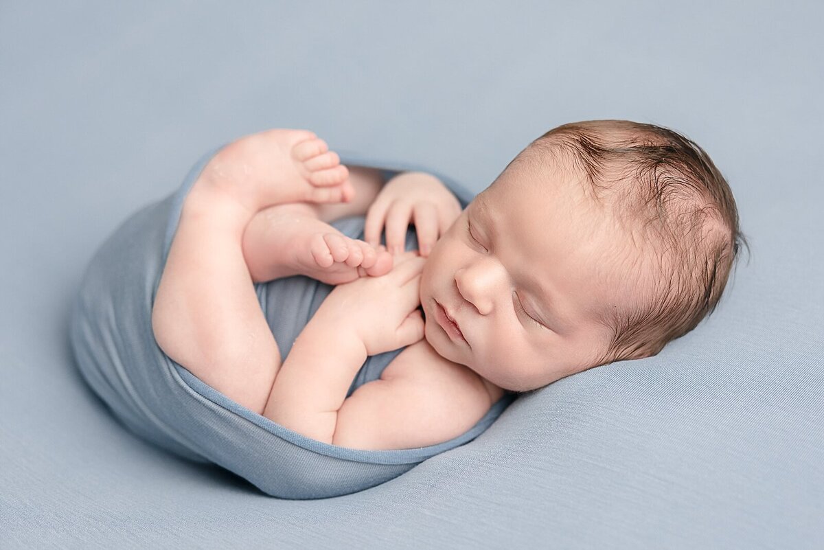 baby boy laying on back wrapped in blue blanket for his portland baby photography session with Ann Marshall