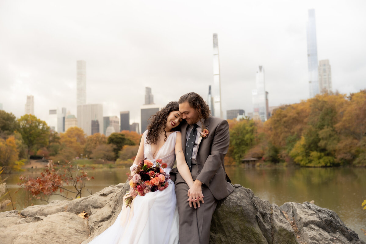 The couple standing close together surrounded by Central Park’s glowing fall foliage.