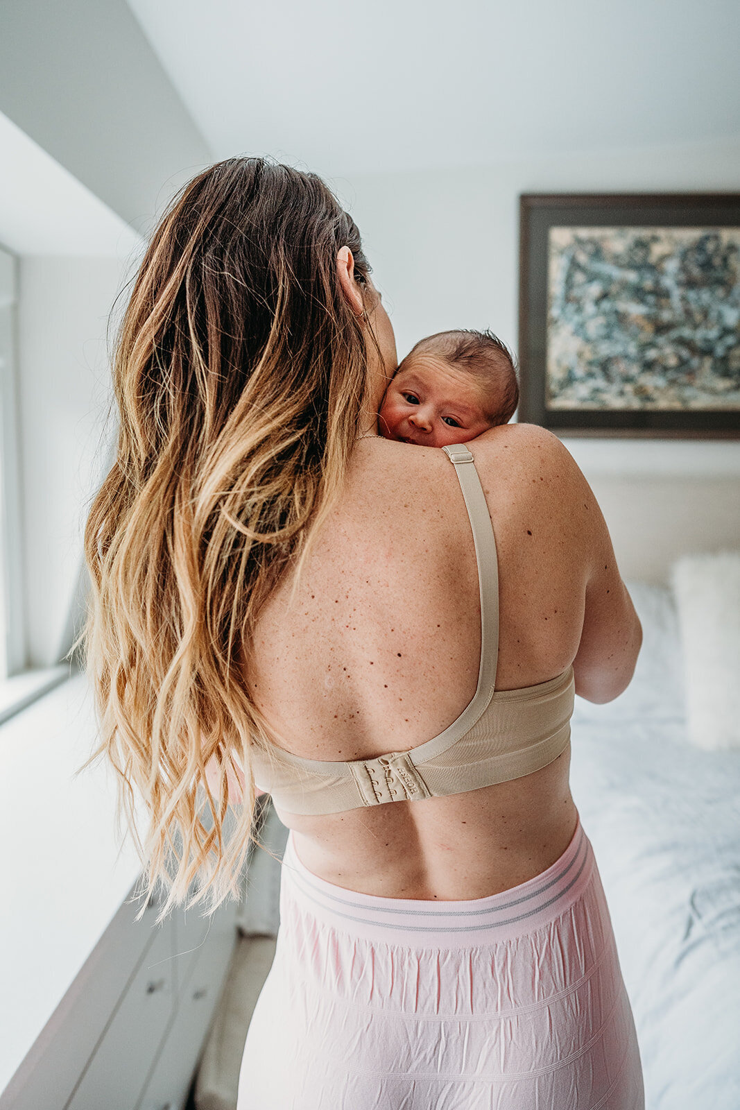 post partum mom in pink underwear and a bra holds newborn over shoulder