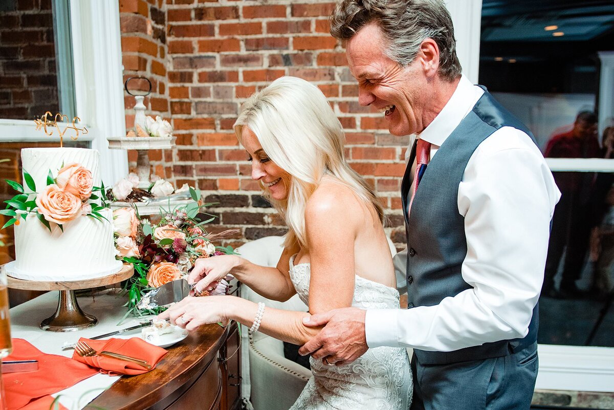Newlyweds cutting wedding cake with brick wall behind them