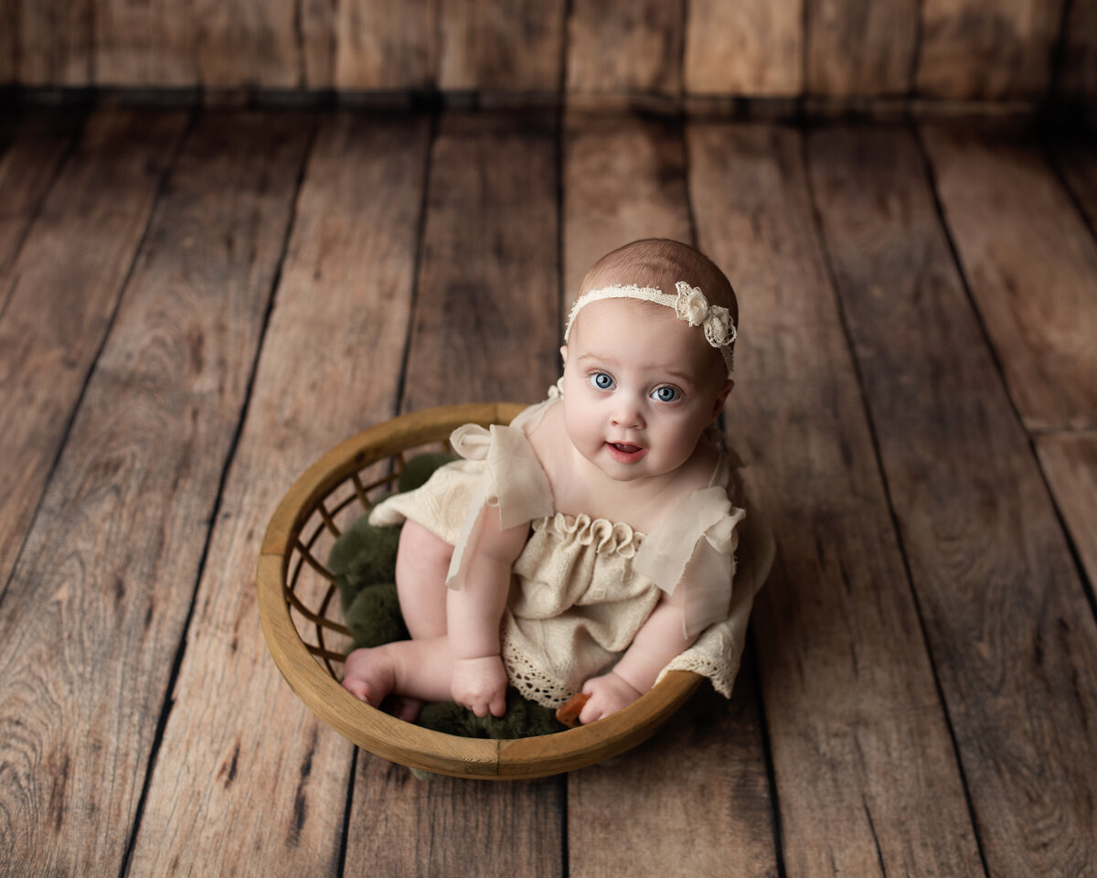 Milestone baby girl portrait in vintage basket with wooden backdrop—styled with heirloom textures and charm.