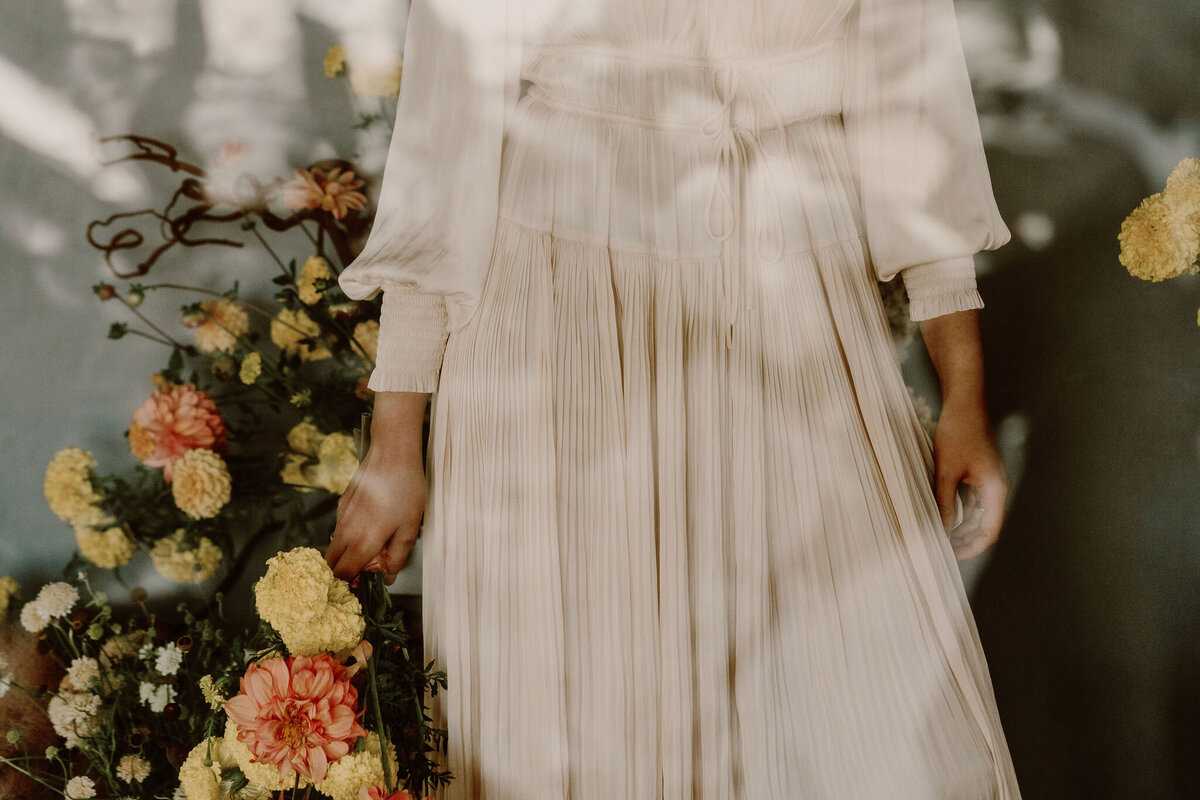 Wanaka Bride in cream dress holding an orange and yellow flower bouquet on her wedding day.