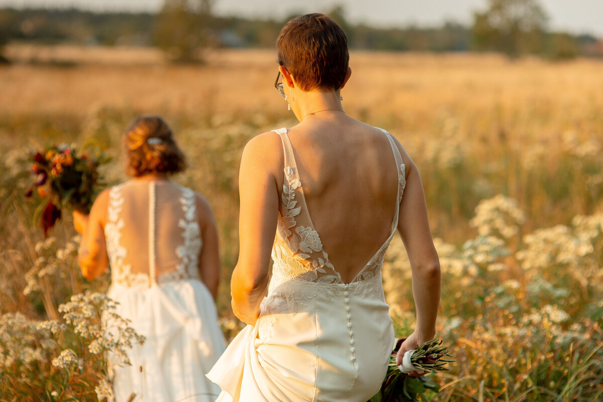 Two brides walk through a field at sunset.