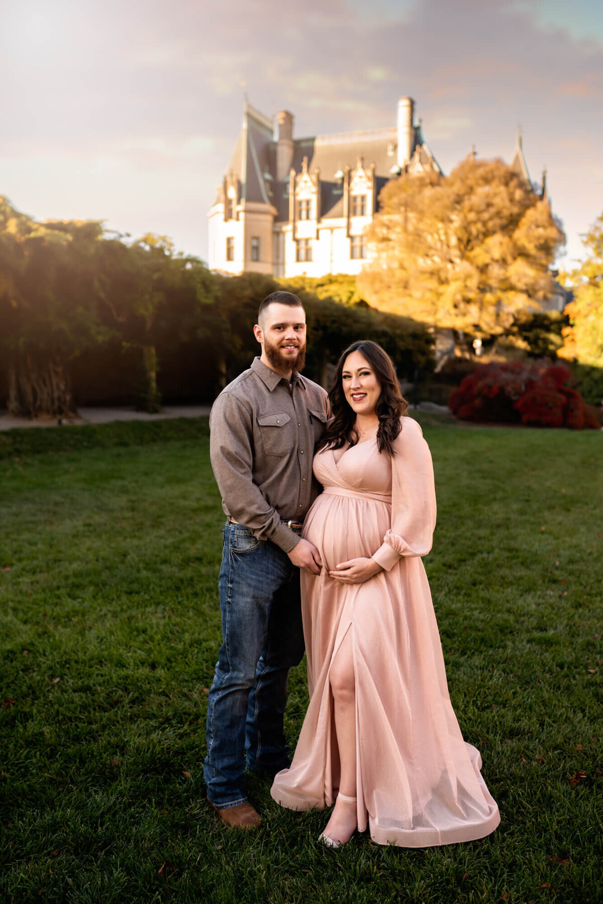 A beautiful expecting mama in an elegant pink dress smiles with her husband during  a portrait session with an Asheville Maternity Photographer