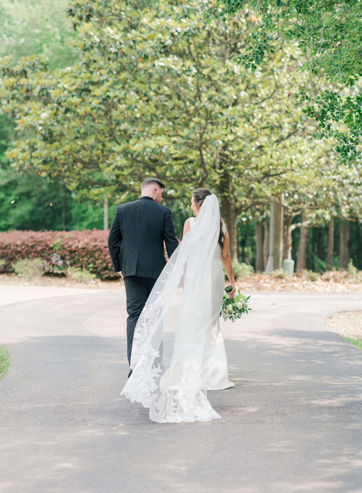 Bride and groom walking away from camera holding hands and bouquet