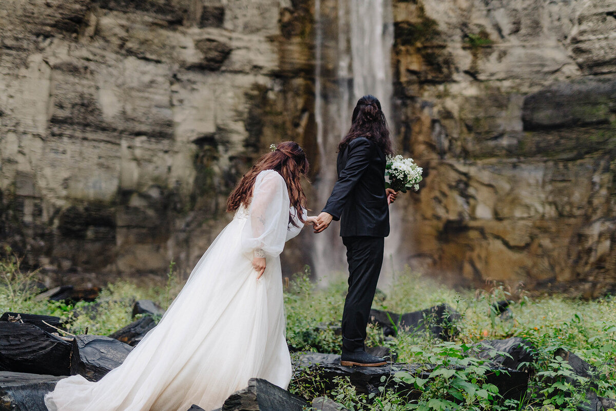 Bride and groom walking along holding hands with a view over Finger Lakes, NY