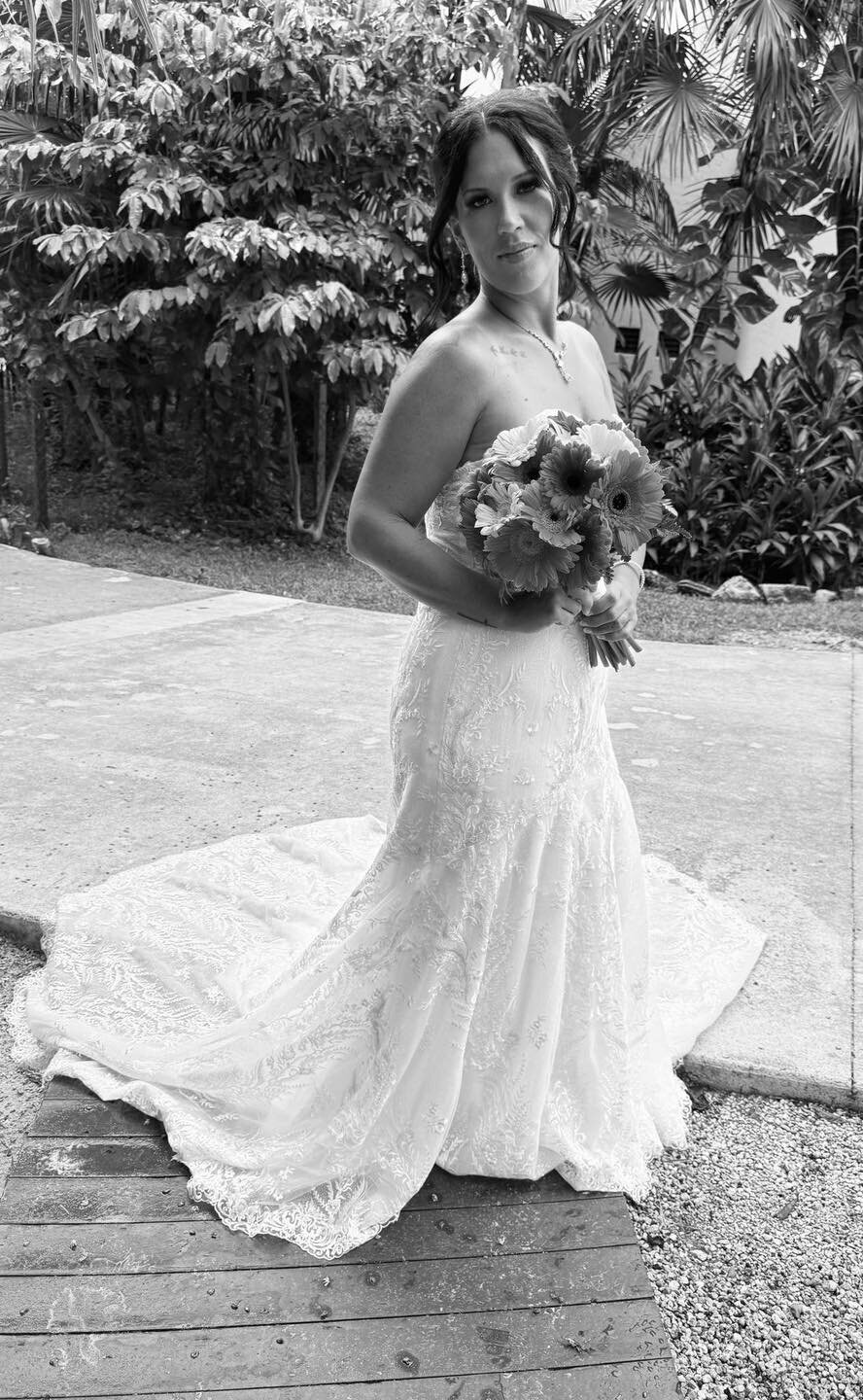 Bride holding a bouquet while wearing a lace fitted wedding gown in a black-and-white photo