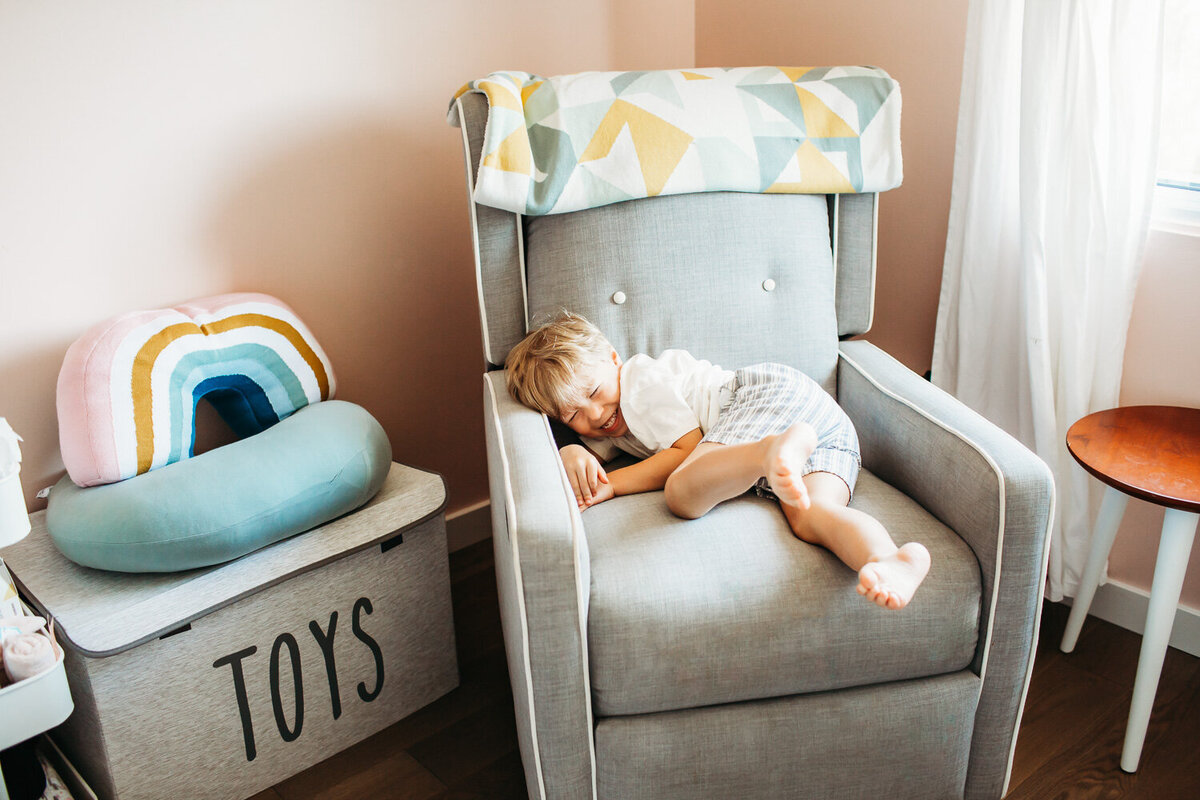 giggling little boy laying on rocking chair in sisters nursery