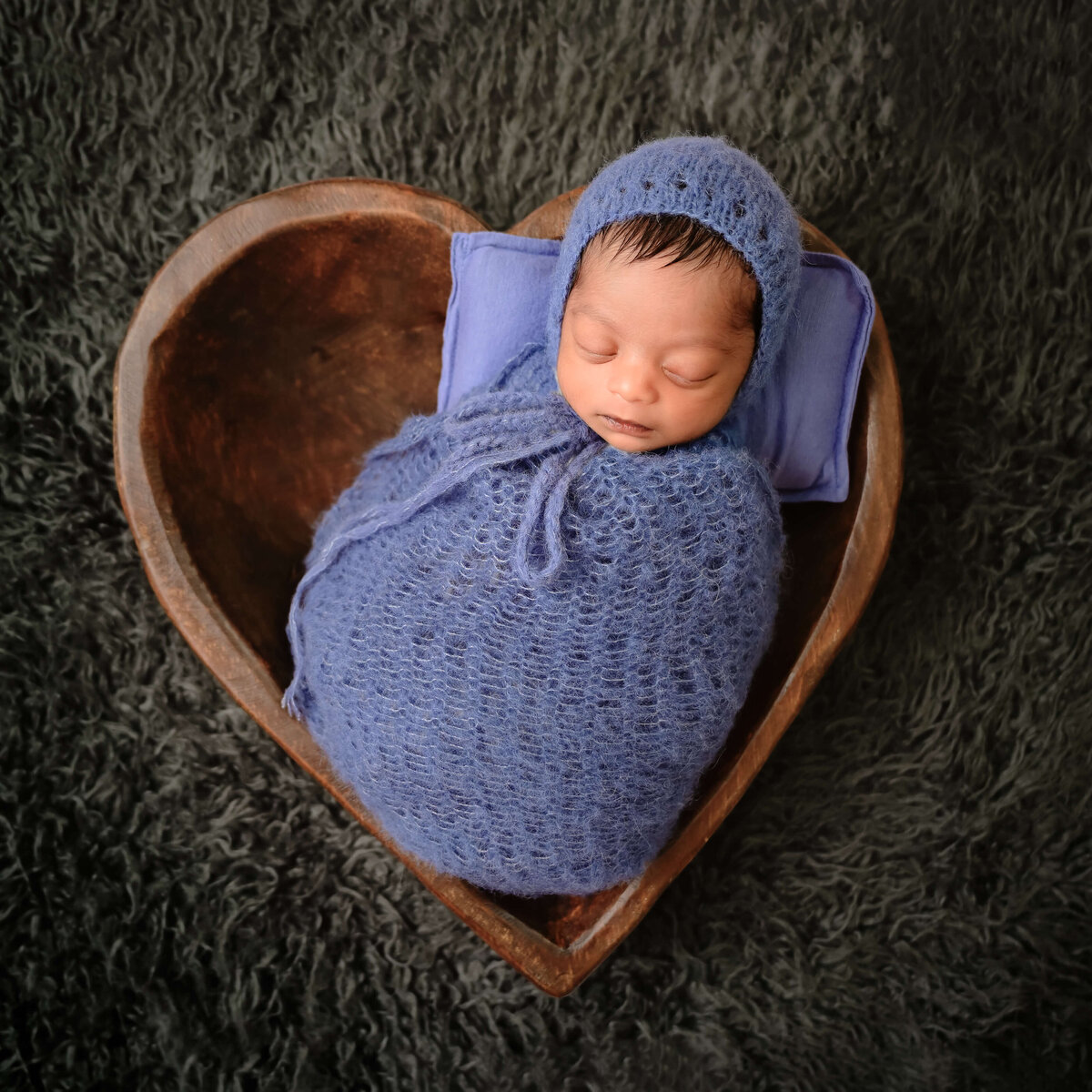 A baby boy wrapped in blue  sleeping in a heart shaped bowl during his Kitsap County, WA in home newborn photo session.