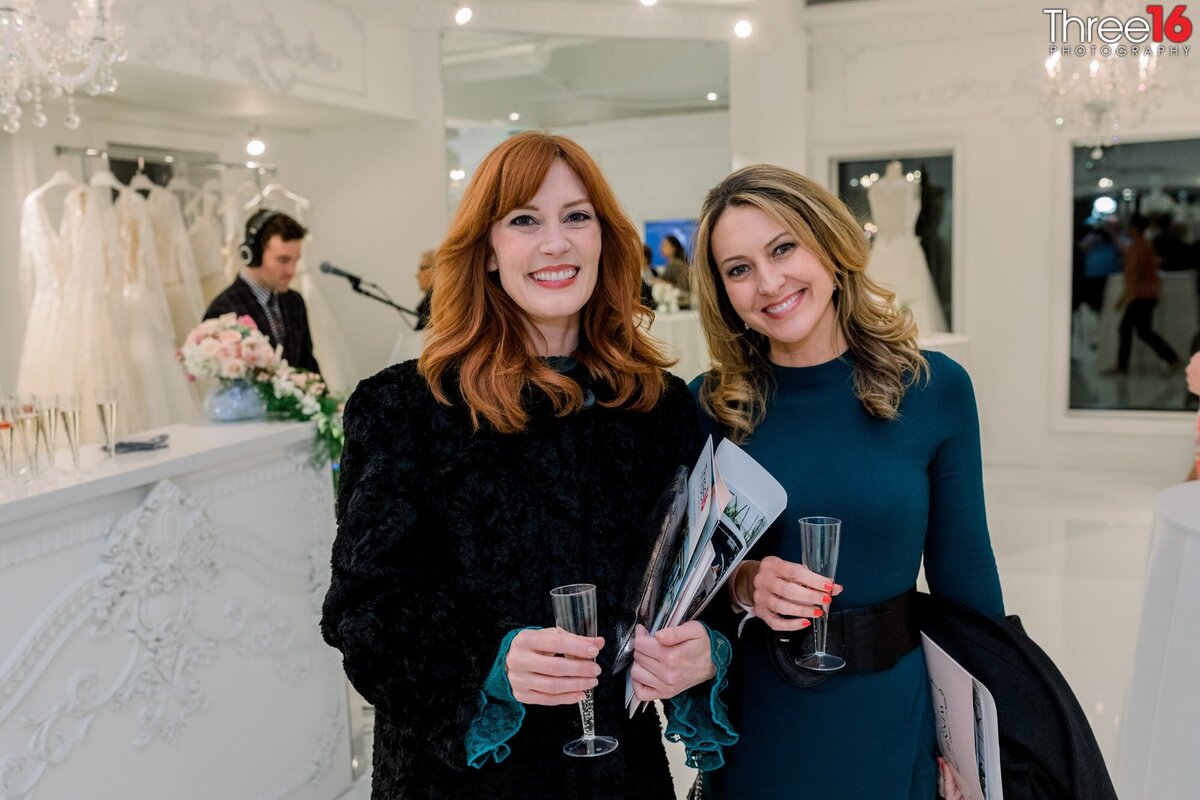 Two ladies pose together at a boutique premier with a DJ in the background