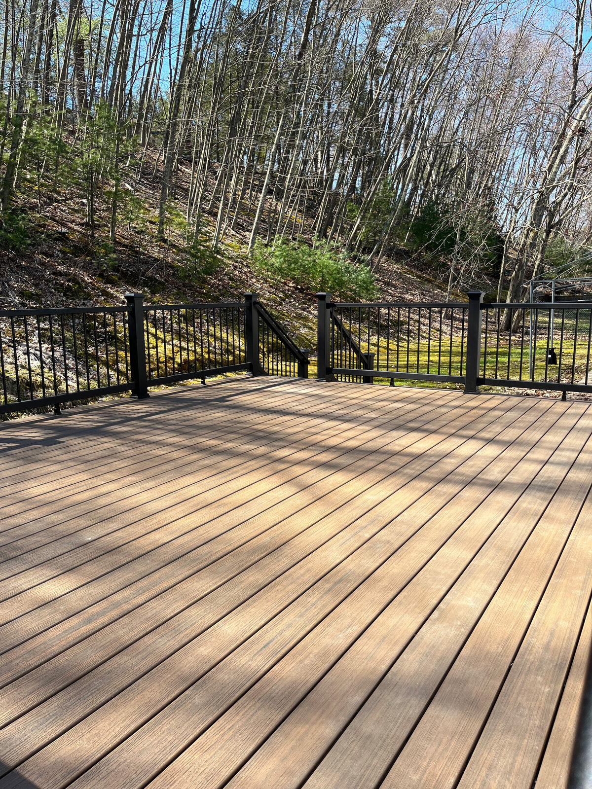 A dark aluminum railing on a darker composite deck in a yard with a hill built by a Marlborough MA Deck Contractor