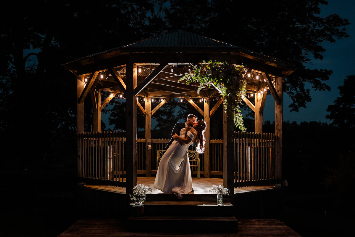 Creative night time photo of groom dipping bride in gazebo