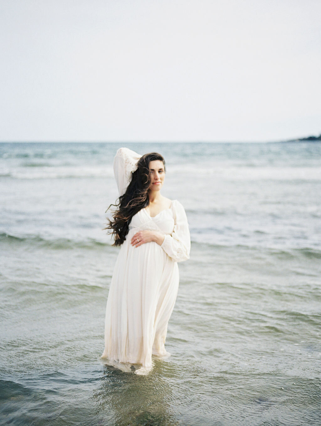 Richmond maternity photography | Film image of a pregnant mother in a lace dress standing in the ocean and holding her head by Jacqueline Aimee Portraits