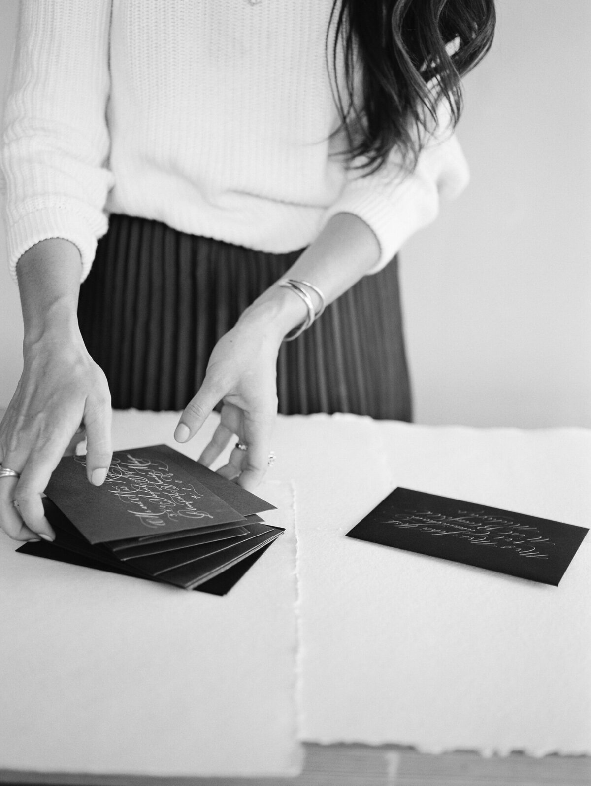 calligrapher, woman artist lifts stack black envelopes, gold ink calligraphy, stationer brand photoshoot