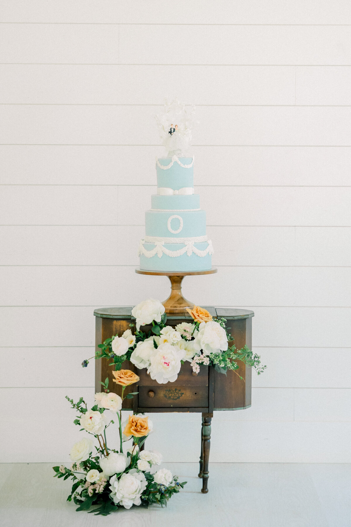 Ivy Rose Barn | A blue and white vintage-inspired wedding cake atop a vintage side table with a stunning floral installation spilling out of the drawers.
