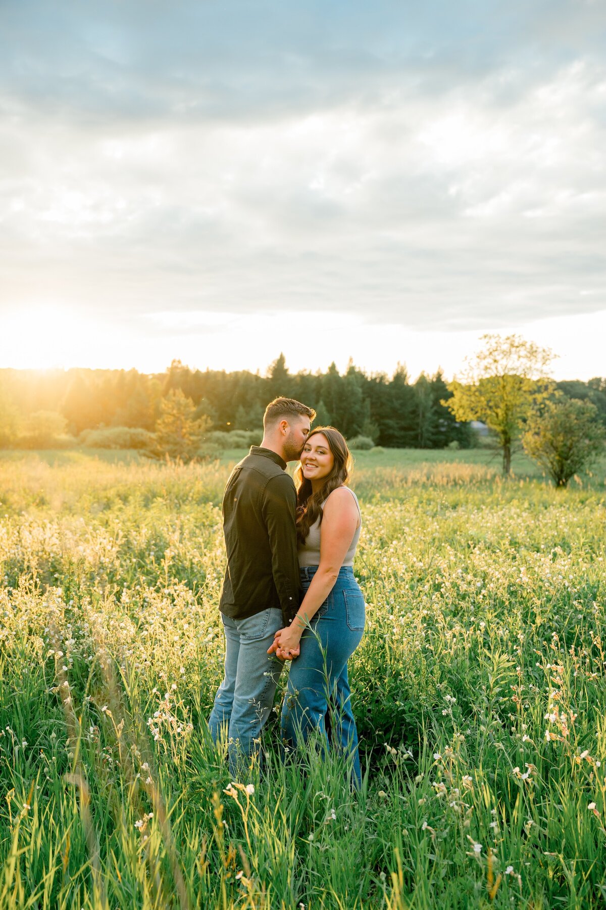 couple in a field holding each other close, the man is kissing the girl on the temple