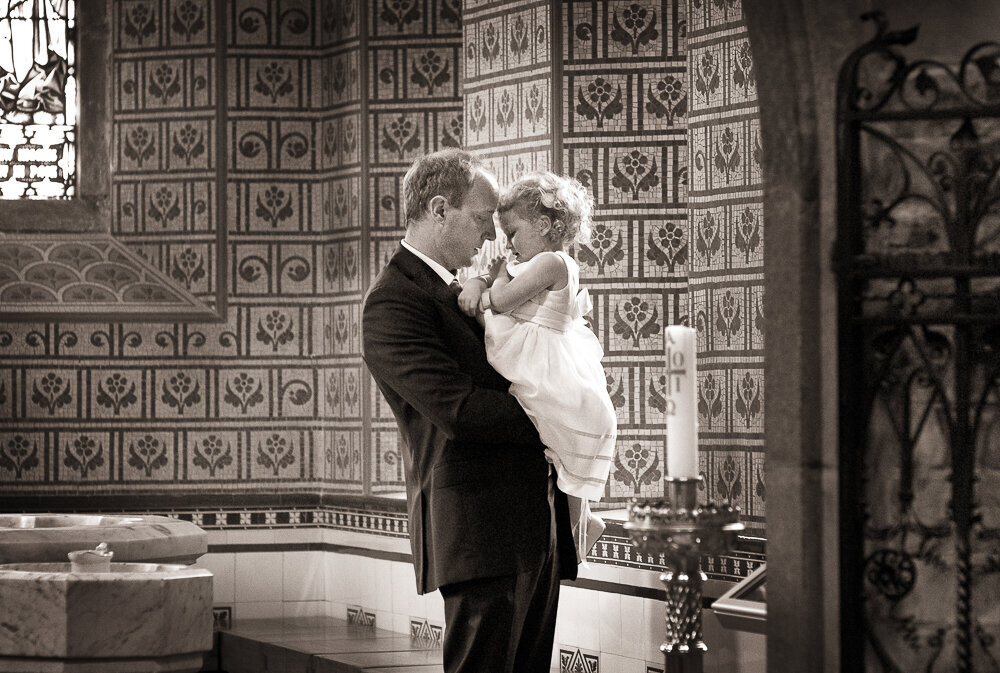 father holding small flower girl beside the baptismal font in Killarney cathedral