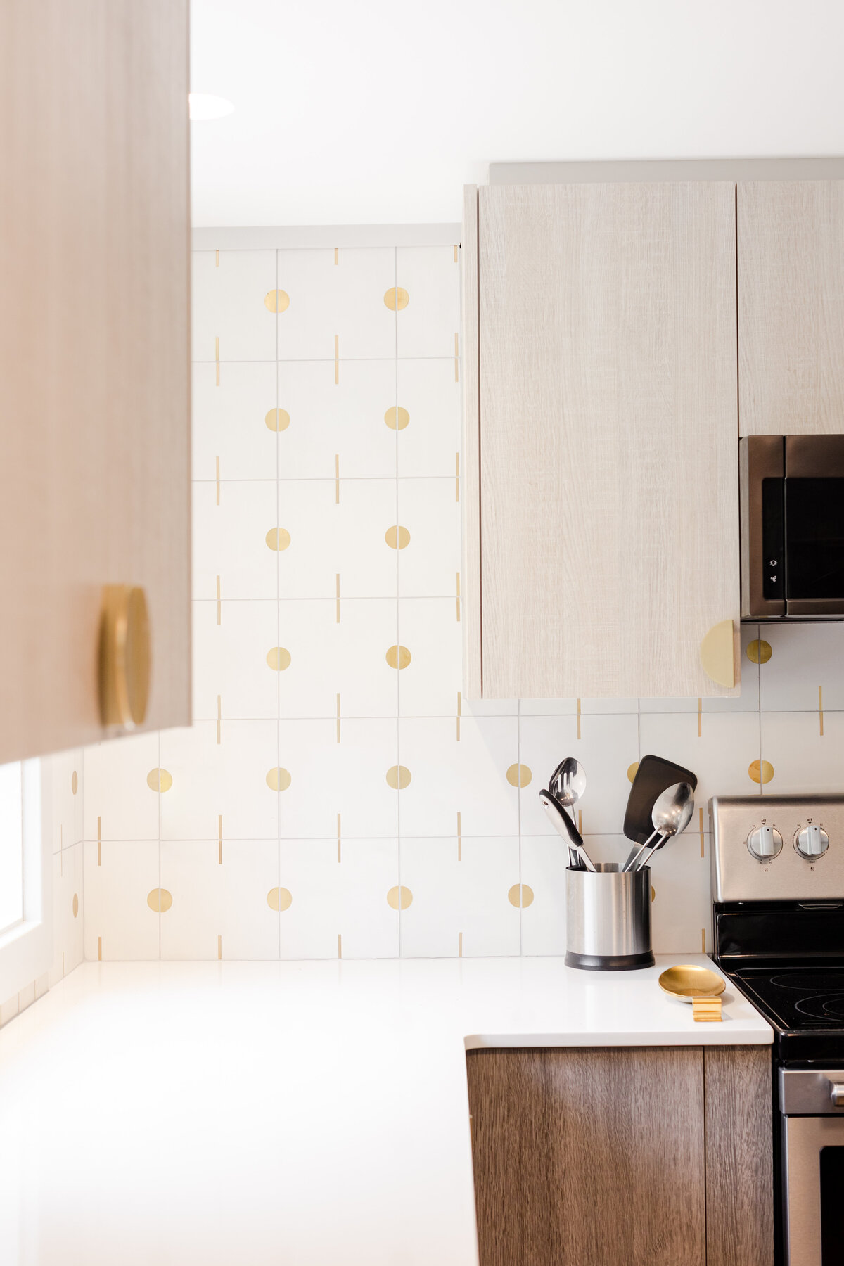 This modern kitchen is designed with a white and gold backsplash, cement tiles with brass inlay, and a white quartz countertop.