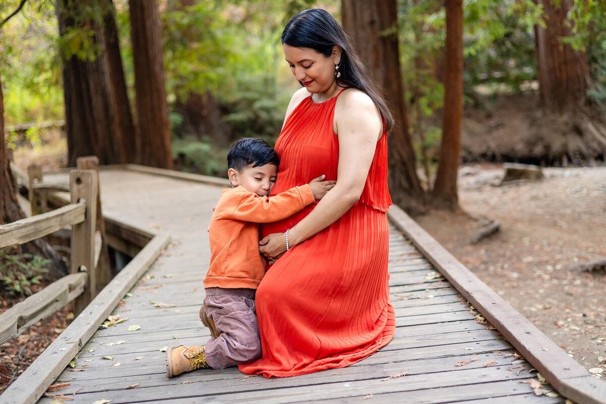 Mother sitting on a wooden bridge, embracing her son and pregnant belly – Ellobelle Photography