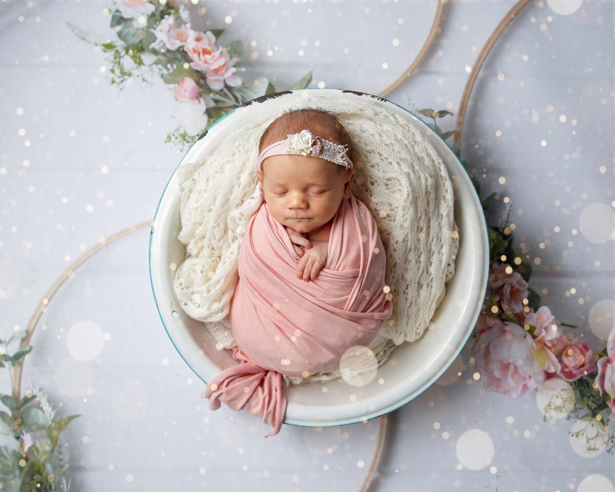 Portrait of a baby girl wrapped in a pink wrap with a cute bow on a background of floral circle reeds