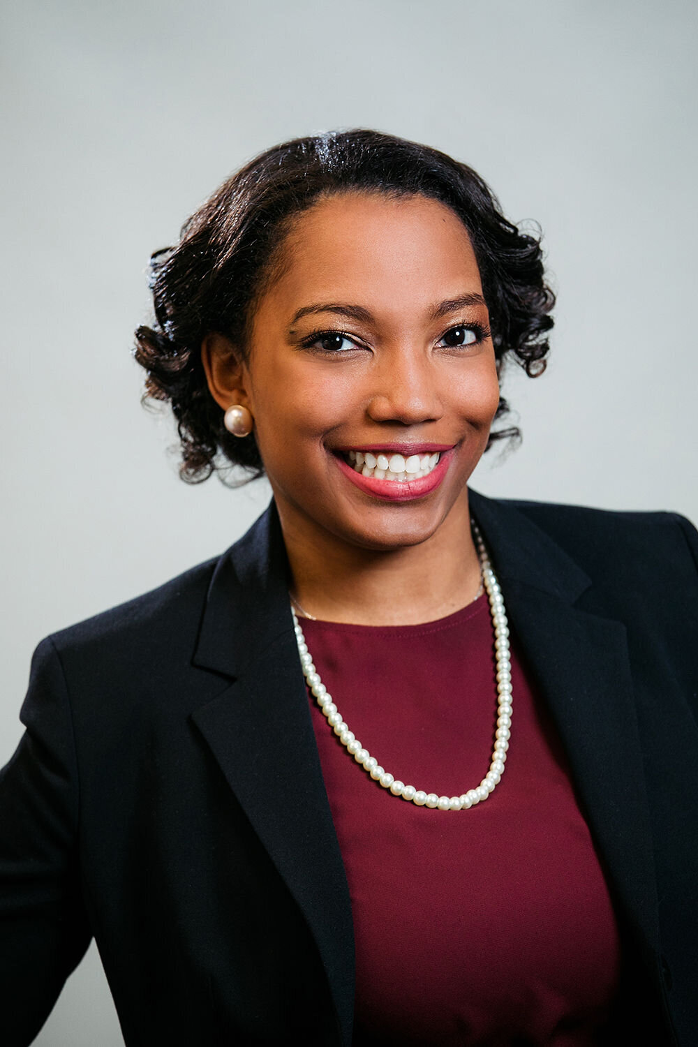 A woman smiles with a maroon shirt and navy blazer.