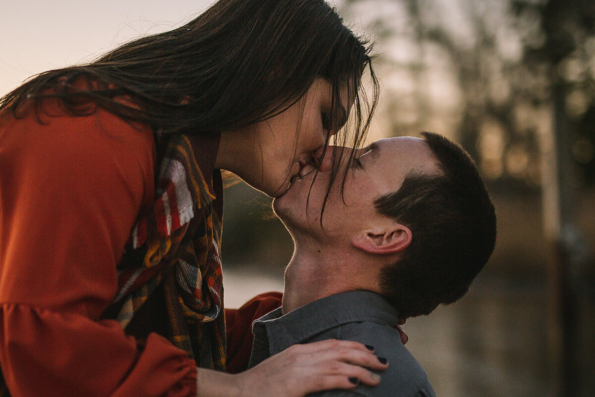 Couple kissing at the lake with autumn tones and hair tendrils blowing gently in the wind,