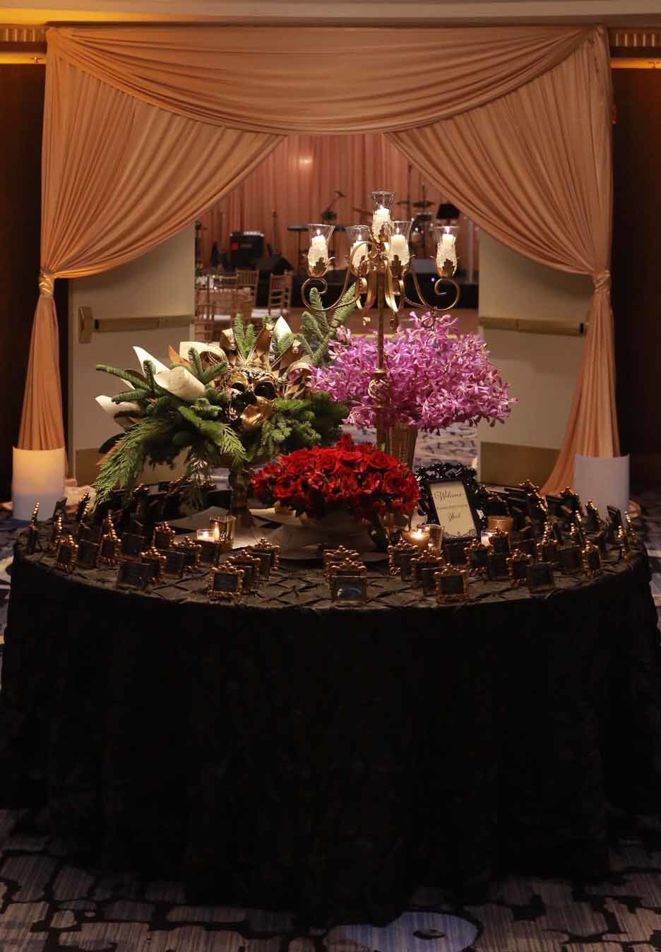 holiday party entrance with vases of purple orchids, red roses, evergreen, and tall candelabra on black table