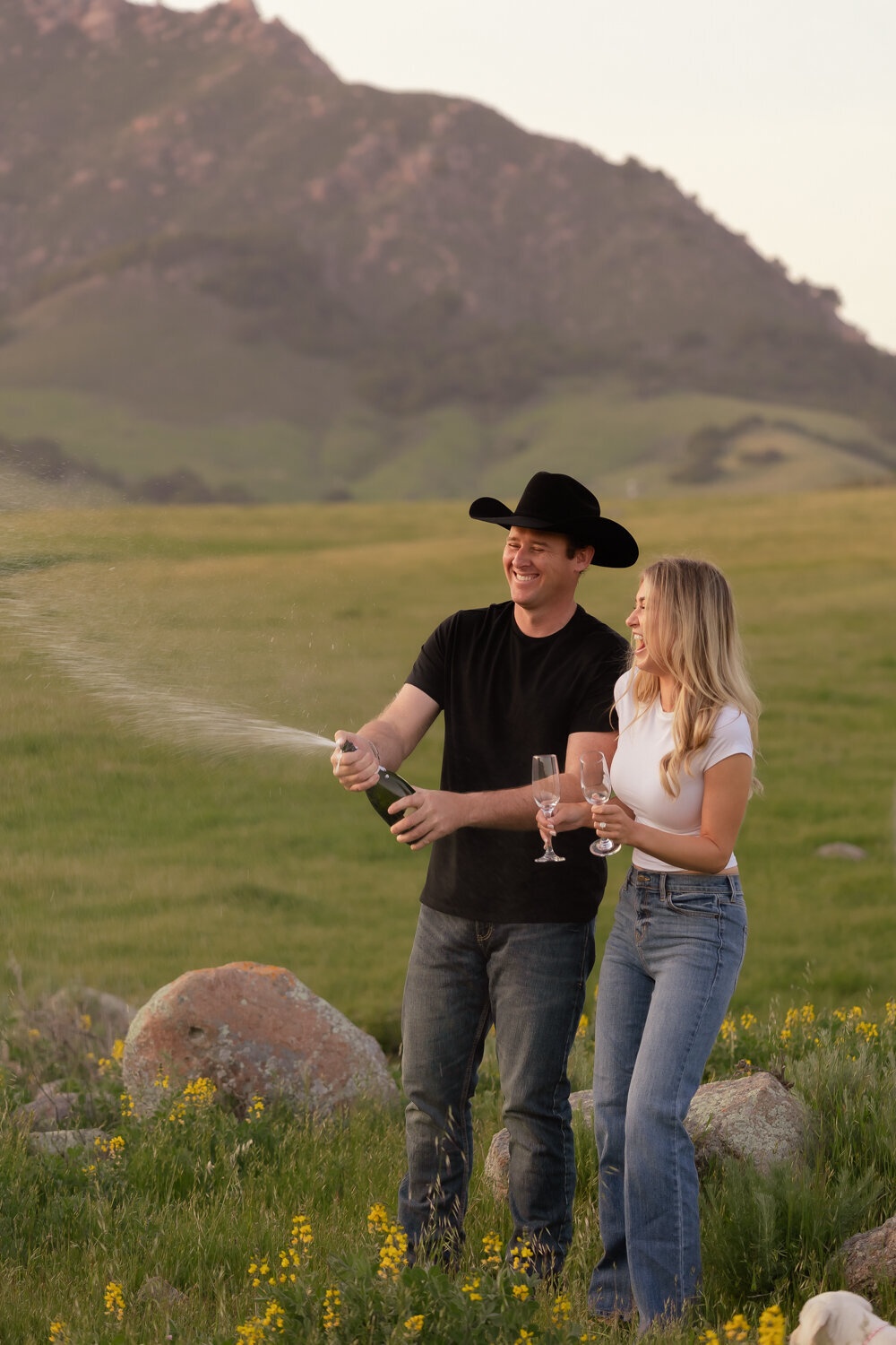 Candid couple during engagement photos in field popping champagne in San Luis Obispo 