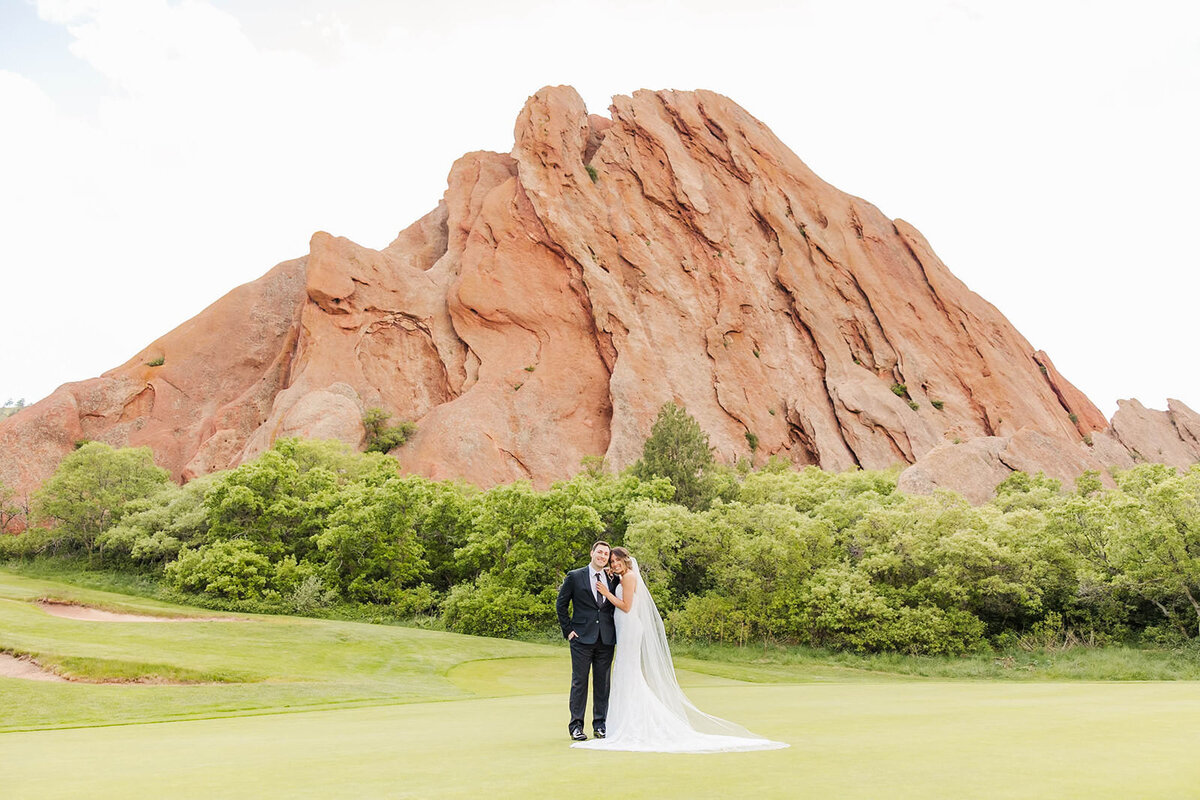 Stunning bride and groom embracing on their wedding day at the picturesque Arrowhead Golf Course in Littleton, Colorado, with striking red rock formations creating a breathtaking backdrop.